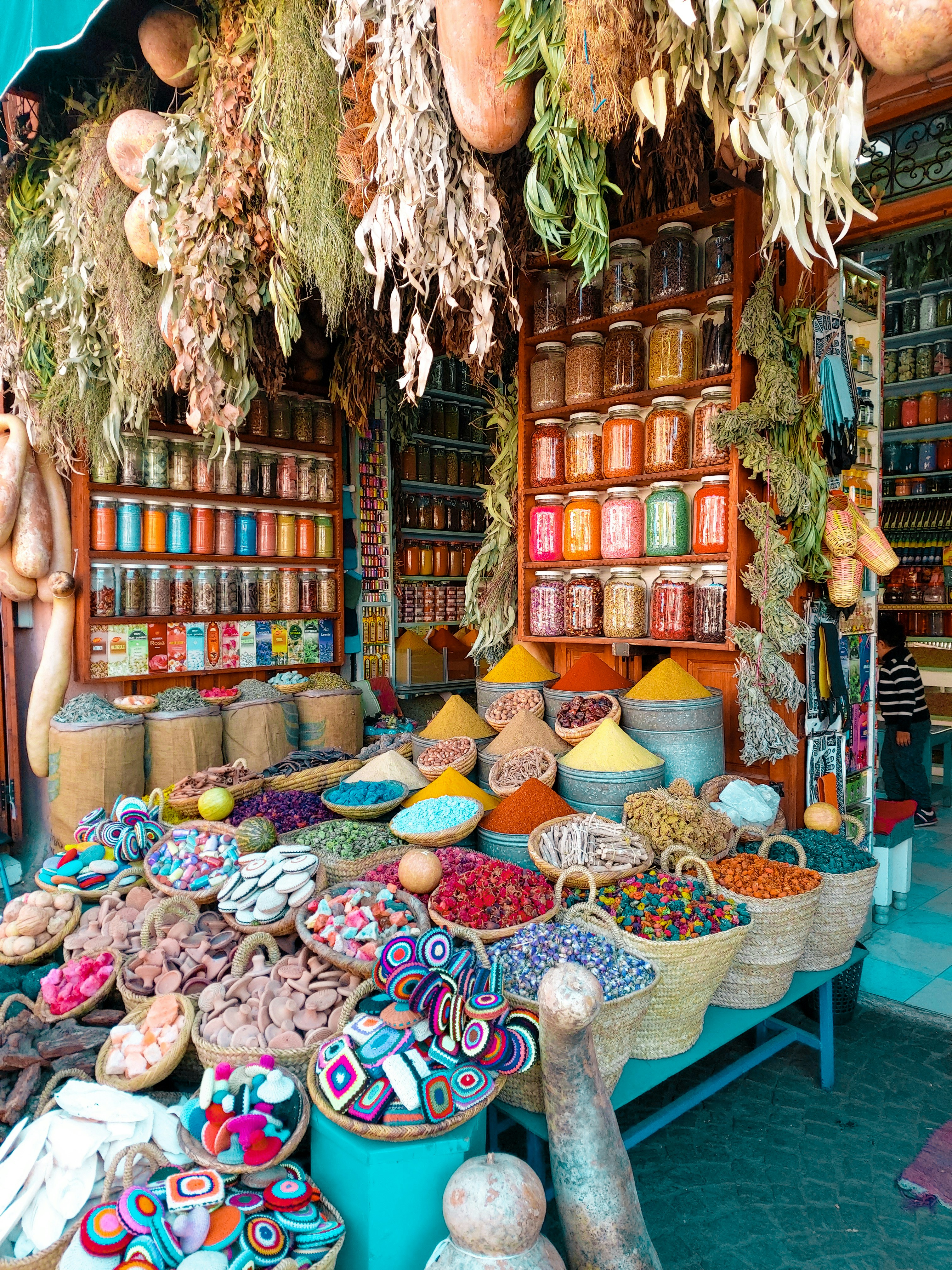 Colorful spice market stall with various spices in sacks and jars, hanging dried herbs, and vibrant textiles in a Moroccan bazaar