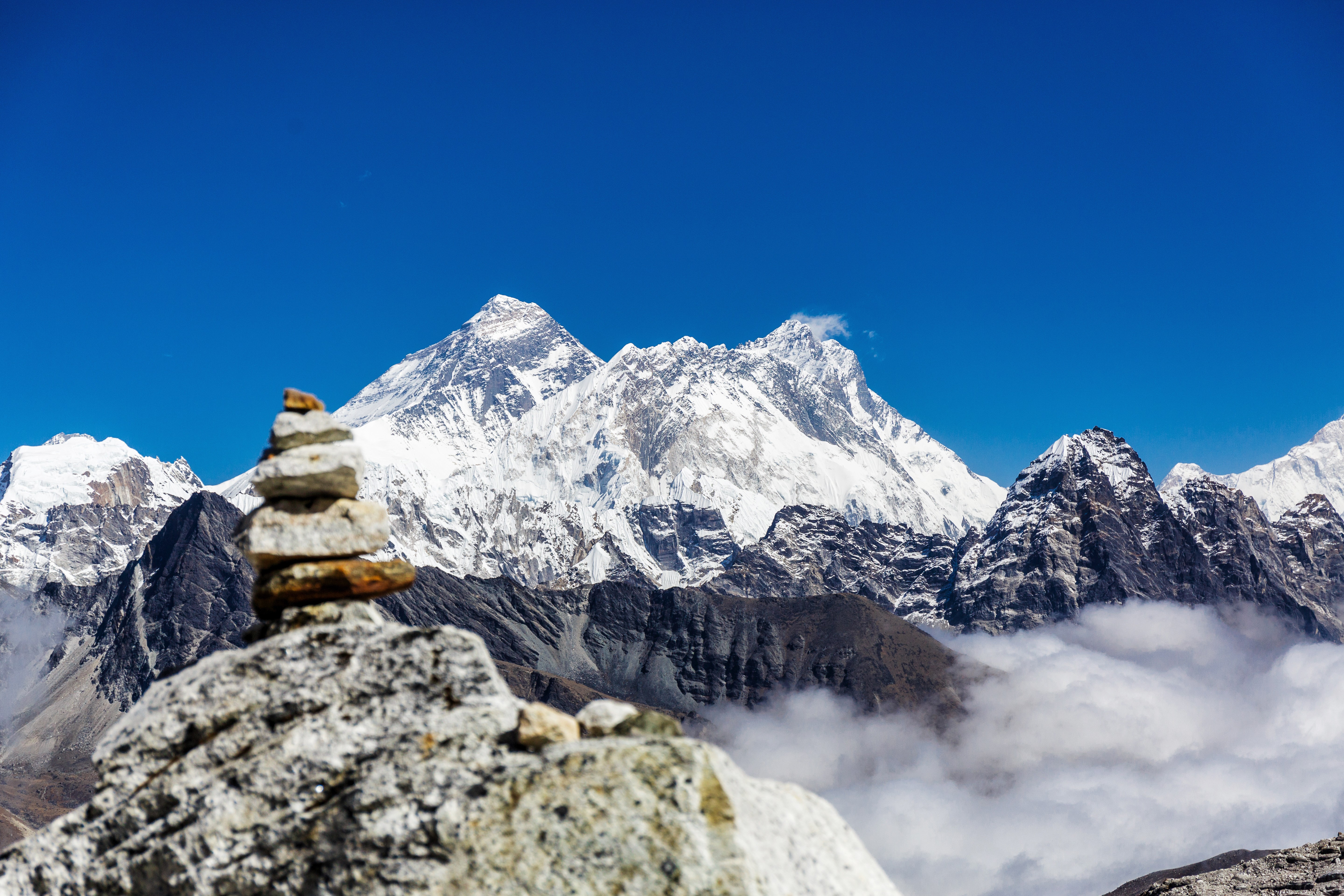 Stacked stones in the foreground with Mount Everest and the Himalayan range under a clear blue sky in the background
