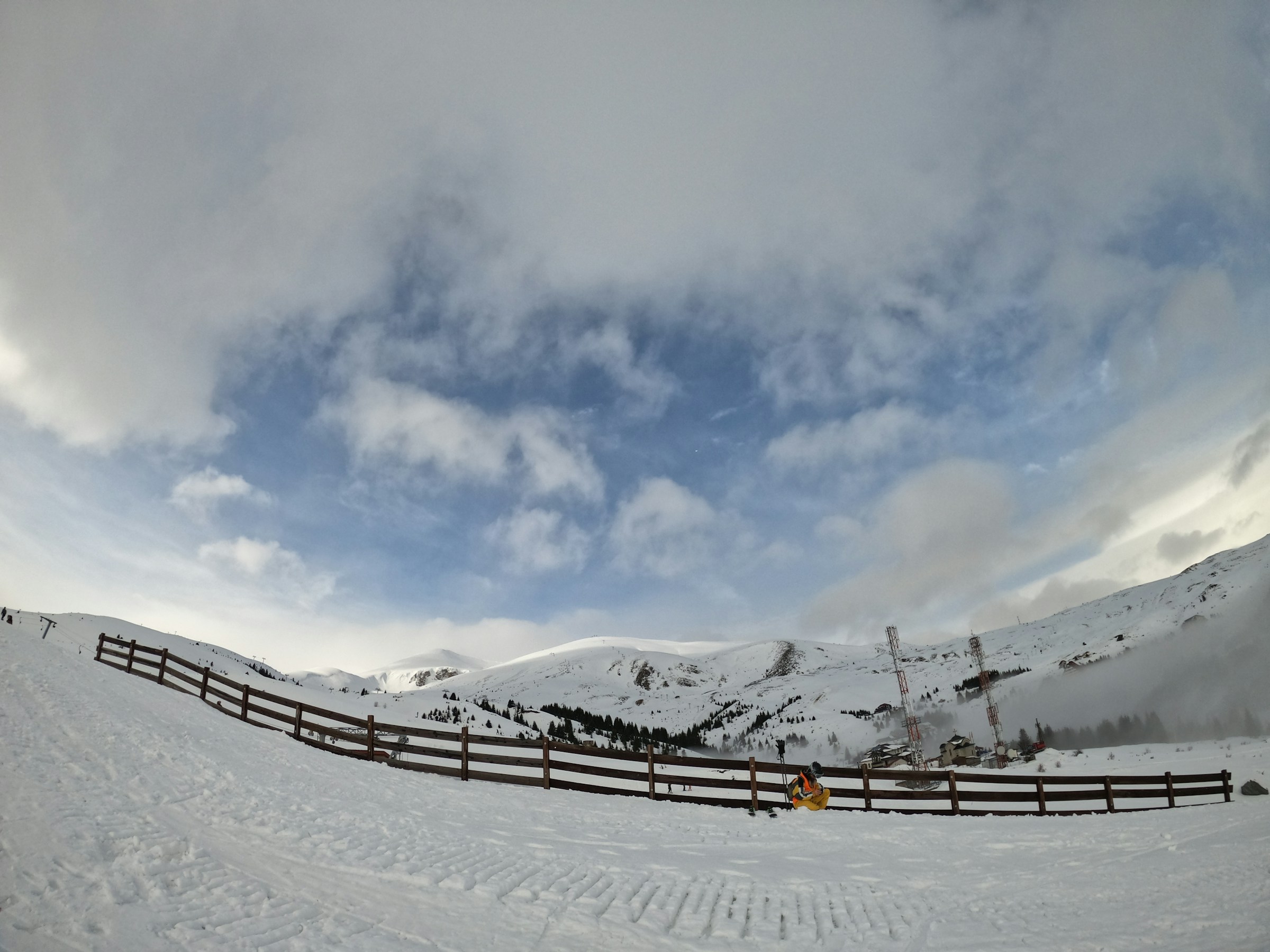 Luminen laskettelurinne, jonka taustalla on puolipilvinen taivas ja vuoret