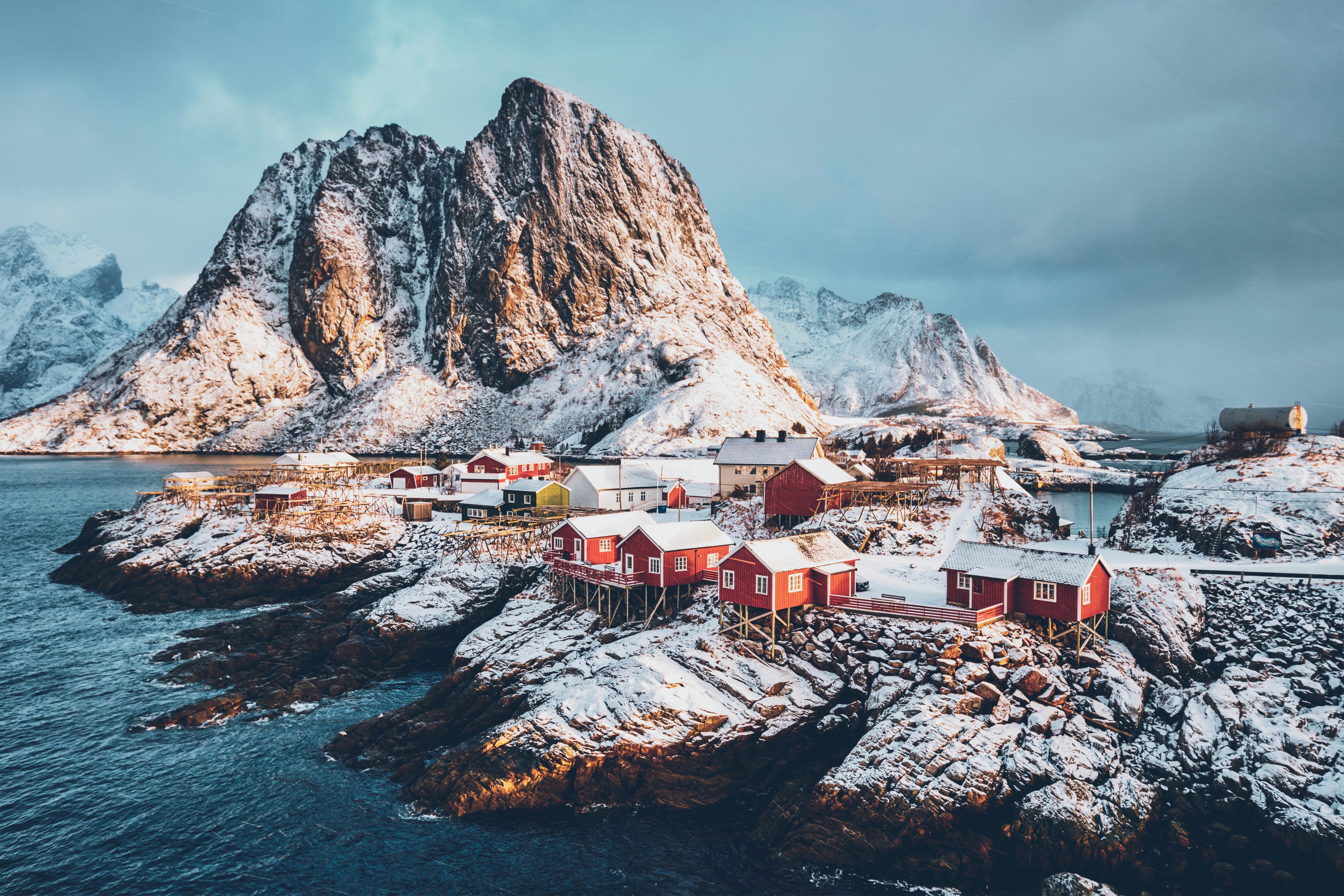 Naturskön vy över en snöig kustby med röda hus och bergig bakgrund i Lofoten, Norge