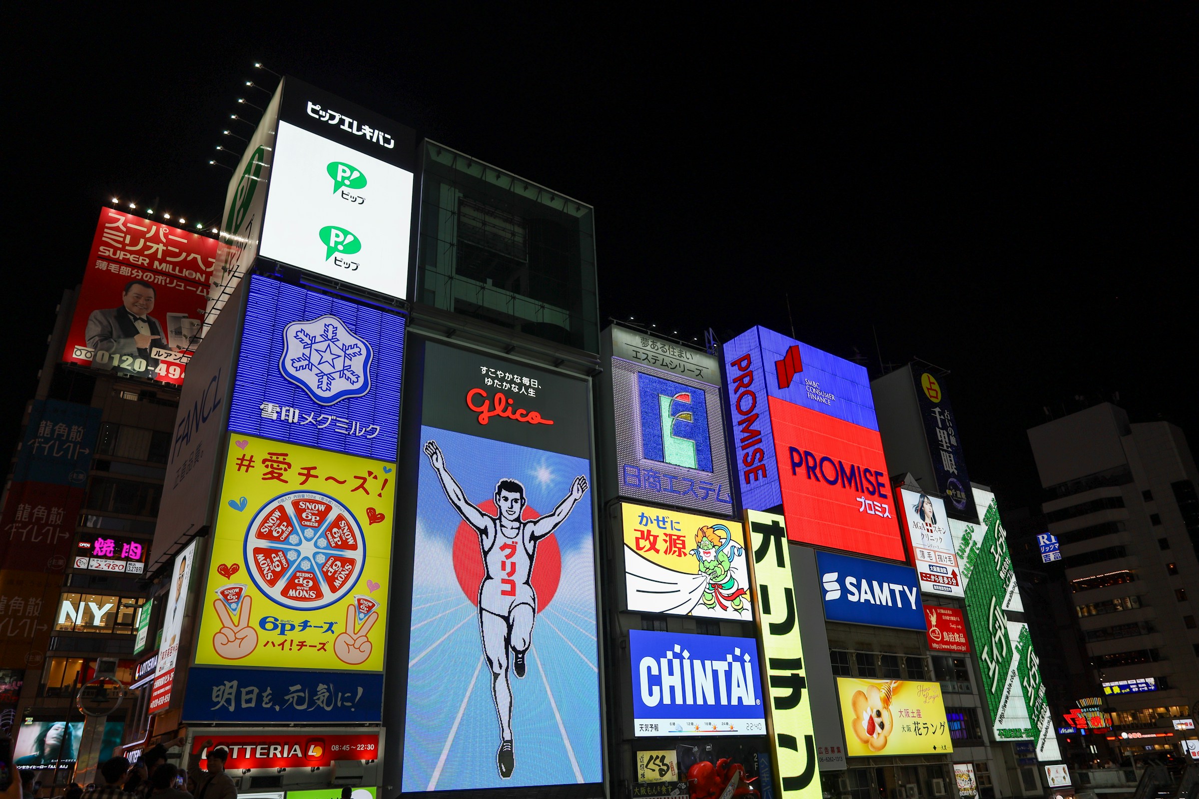 Neonskyltar och reklam på byggnader i Dotonbori, Osaka, Japan, med Glica-löparskylt i centrum, nattvy.