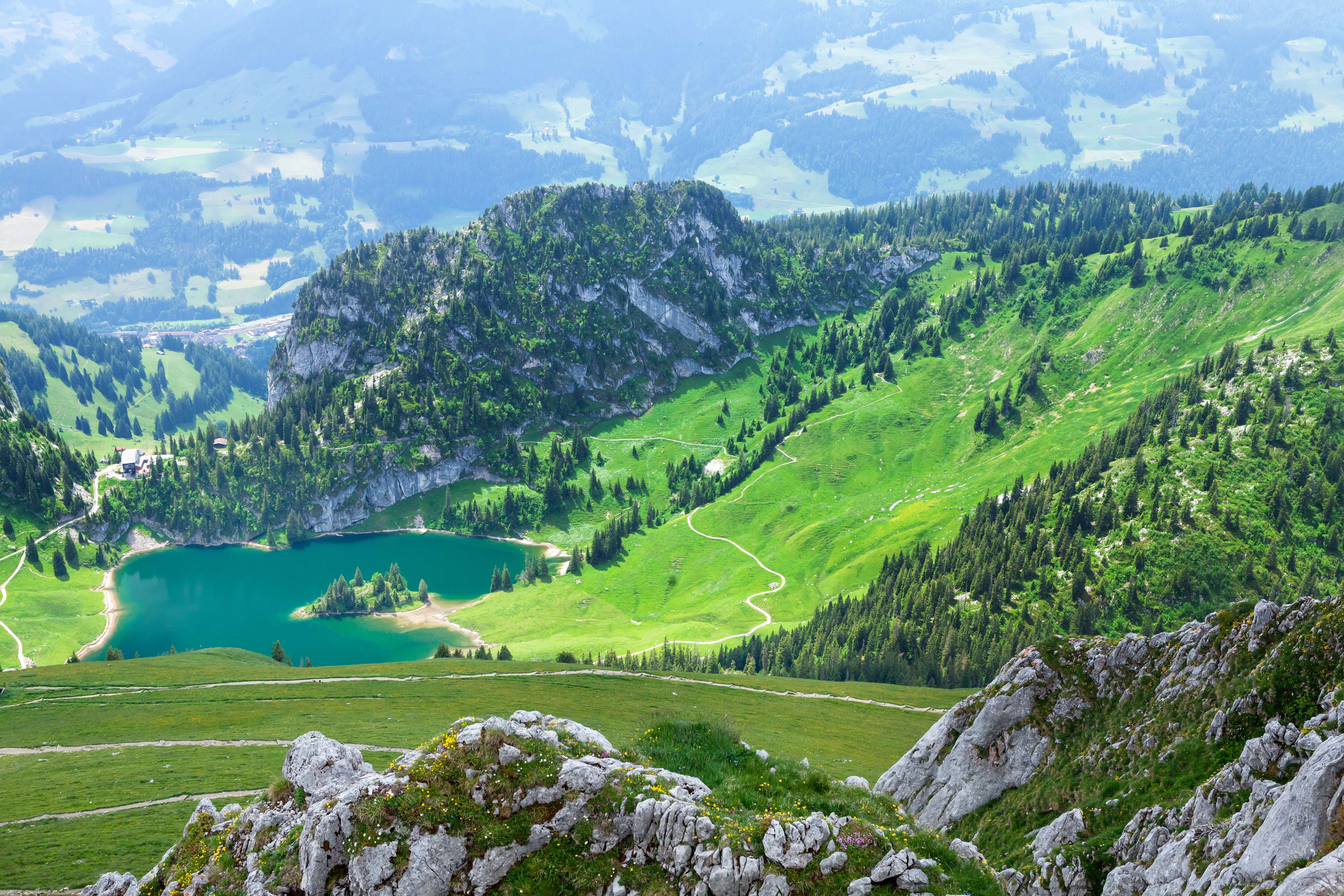 Naturskön vy över frodiga gröna berg som omger en klarblå alpsjö, med steniga klippor och slingrande stigar i en fridfull, naturlig miljö