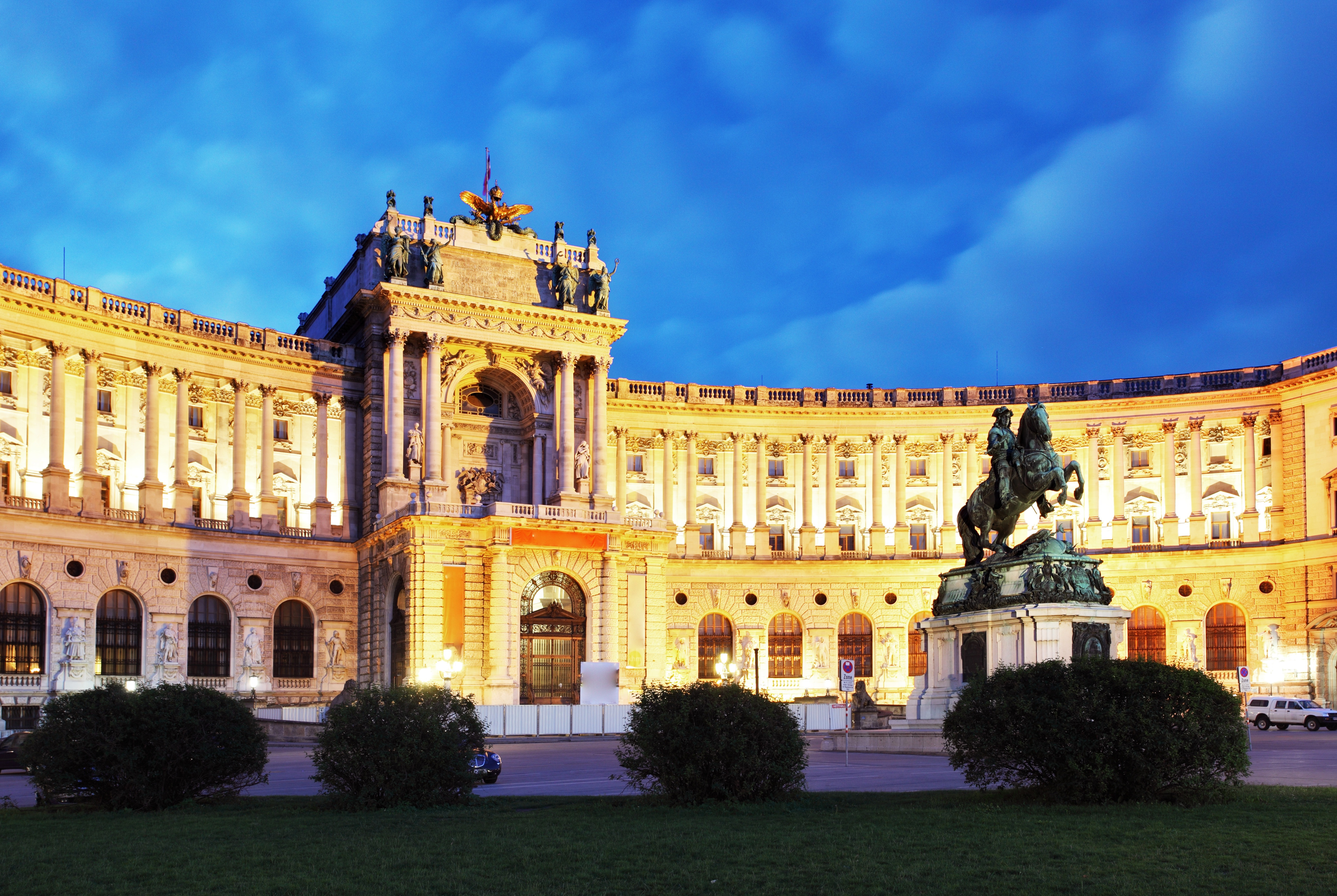 Illuminated Hofburg Palace in Vienna at dusk, showcasing the historic architecture and equestrian statue in the foreground