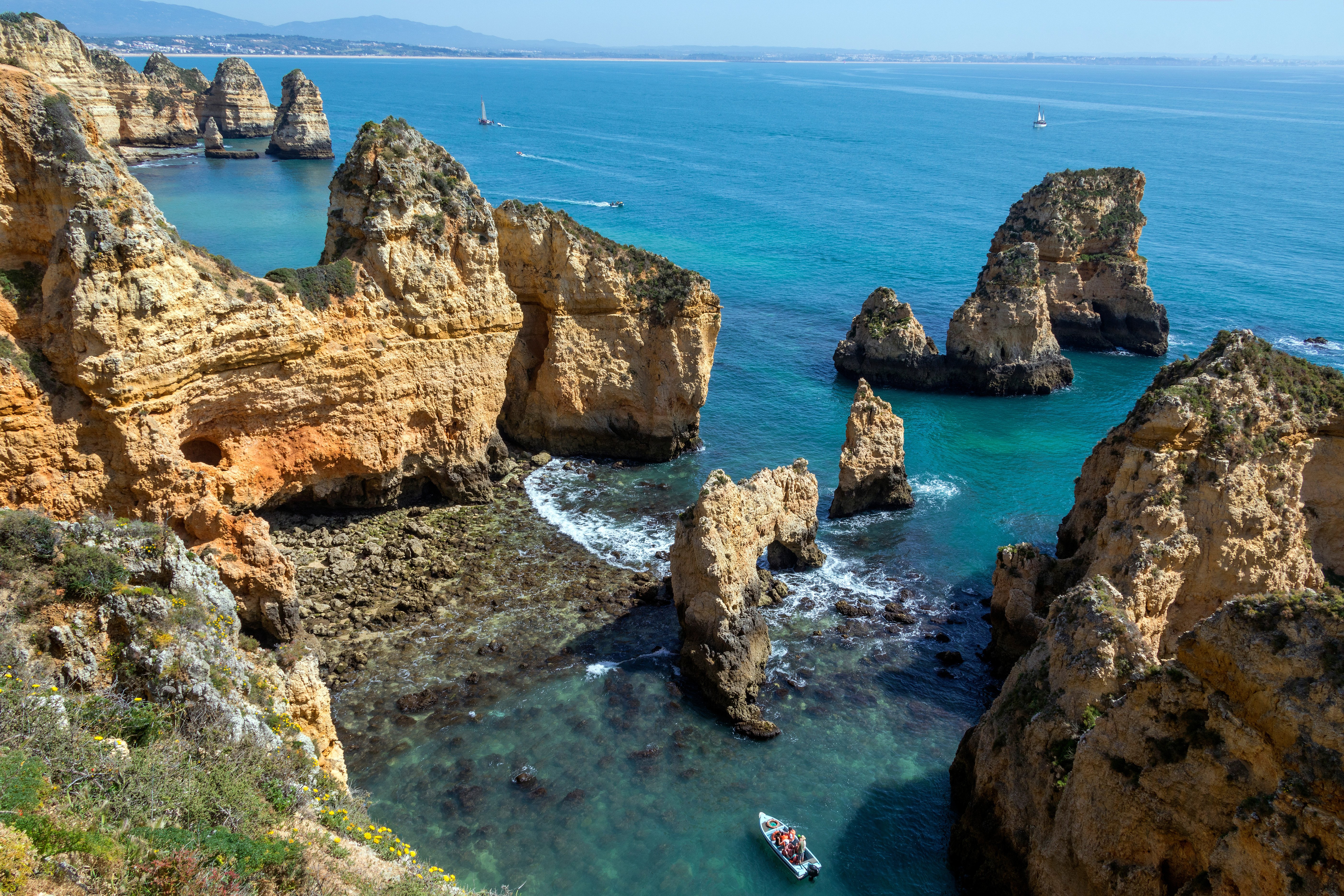Ponta da Piedade -kallioiden maalauksellinen näkymä Lagosissa, Portugalissa, jossa on upeita kalkkikivimuodostelmia turkoosien vesien ympäröimänä, ja veneet sekä etäiset purjeveneet lisäävät viehätystä rannikkoympäristöön