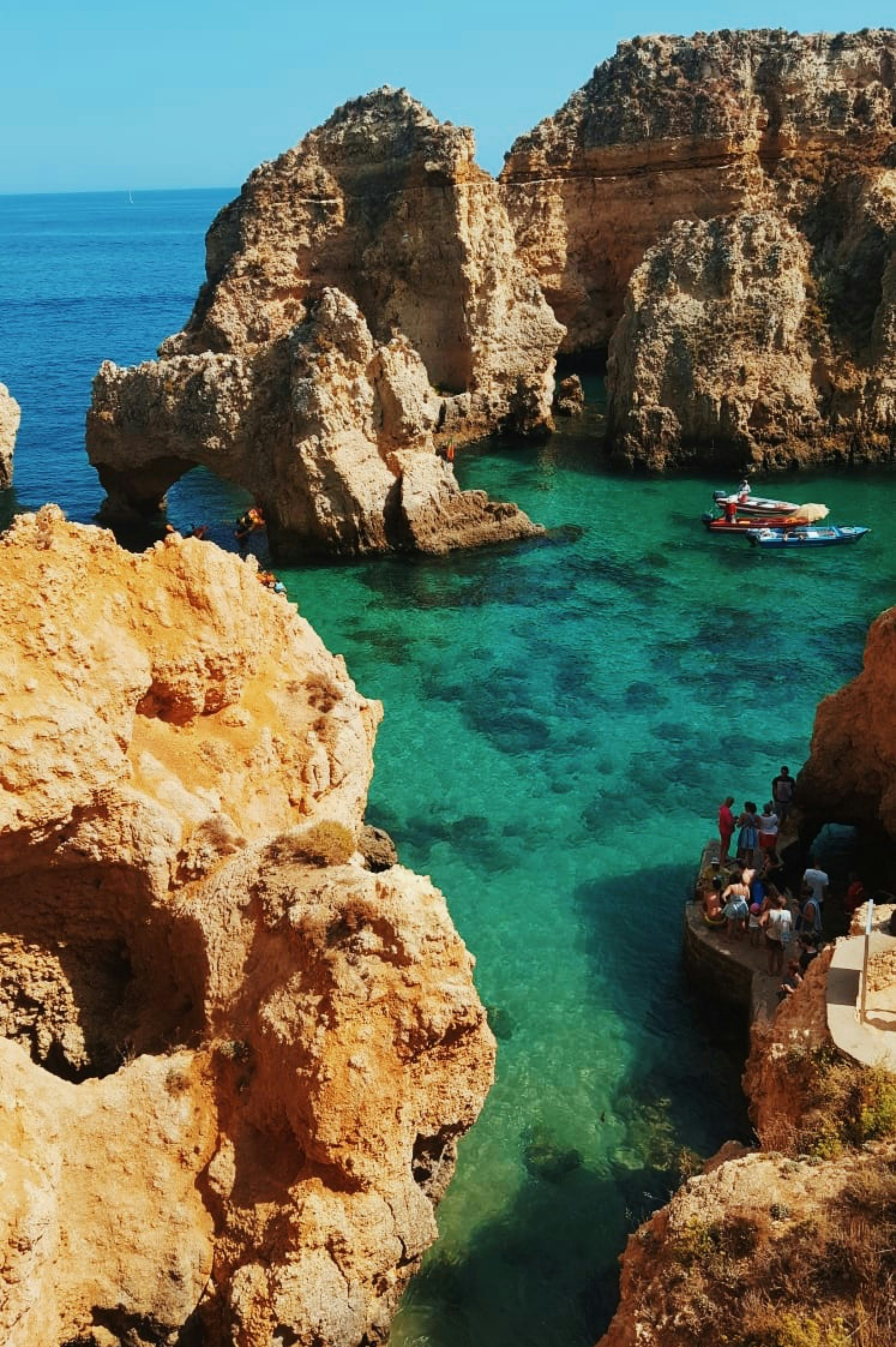 Kuvankaunis näkymä kalliokielekkeistä ja turkoosista vedestä Ponta da Piedadella, Algarvessa, Portugalissa, jossa vene ja turistit tutkivat luonnonmuodostelmia