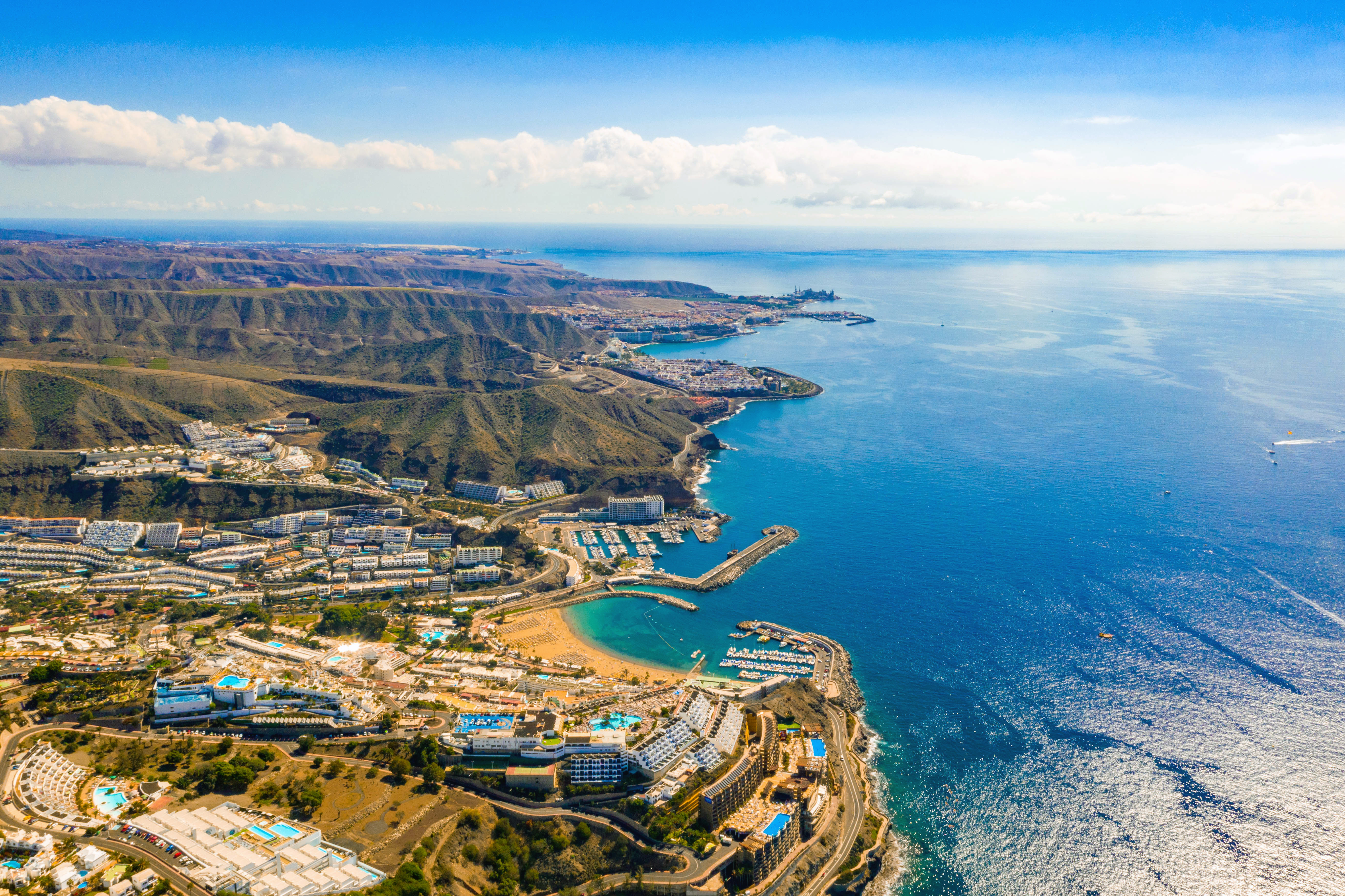 Travel to Gran Canaria - Aerial view of coastline with resorts, beaches, and blue ocean waters under a sunny sky.