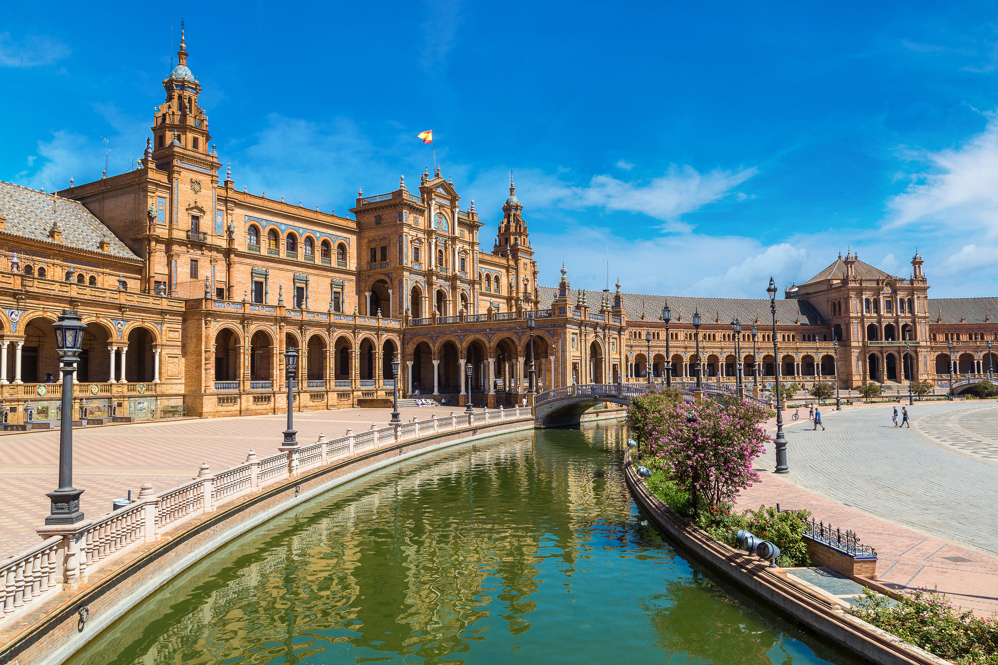 Plaza de España i Sevilla, Spanien, visar upp sin ikoniska arkitekturstil med en omgivande kanal och dekorativa broar under en klarblå himmel
