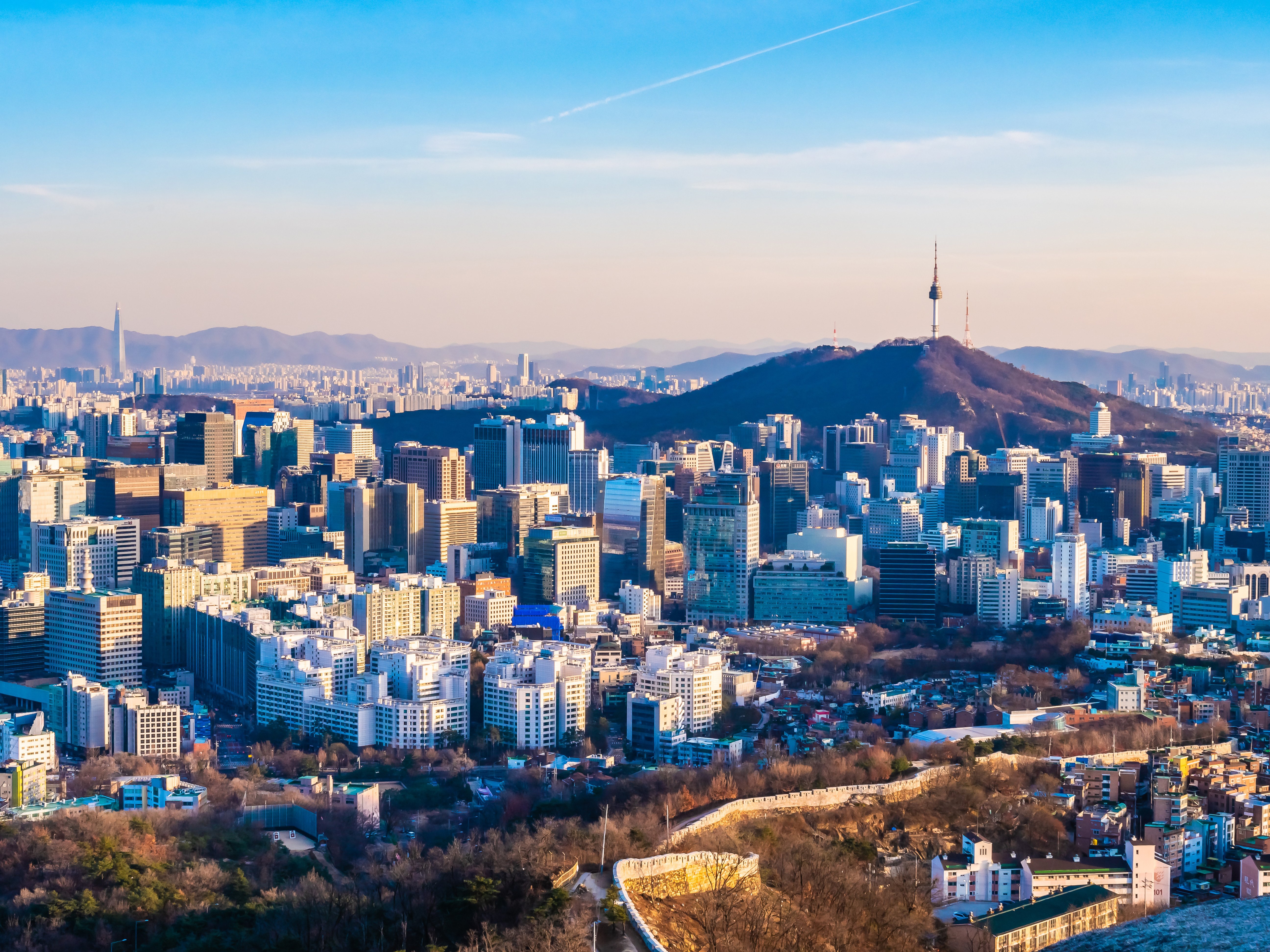 Seoul city skyline with Namsan Tower and mountains in the background, showcasing modern skyscrapers and urban landscape under a clear blue sky