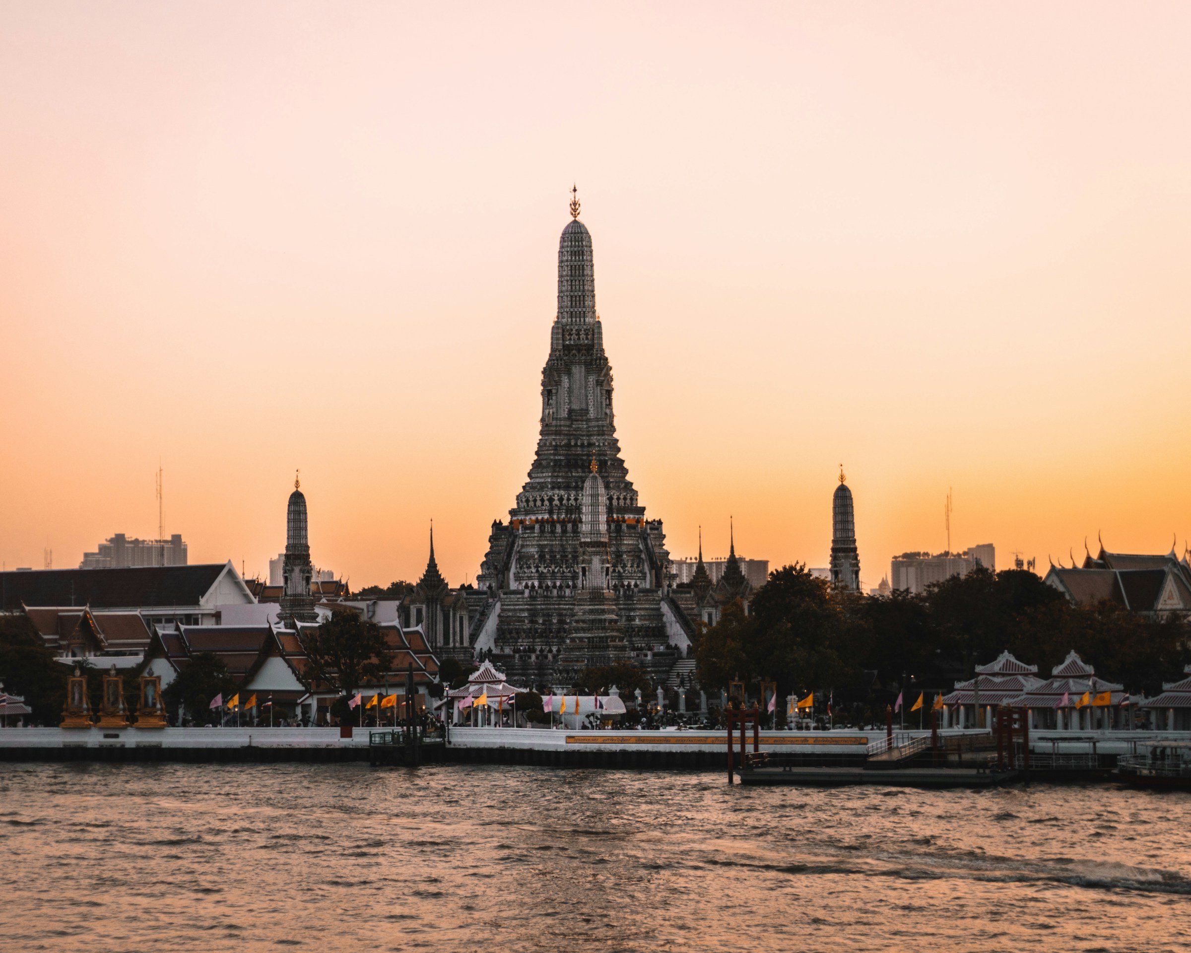 Wat Arun temple silhouetted against a vibrant sunset on the Chao Phraya River in Bangkok, Thailand.