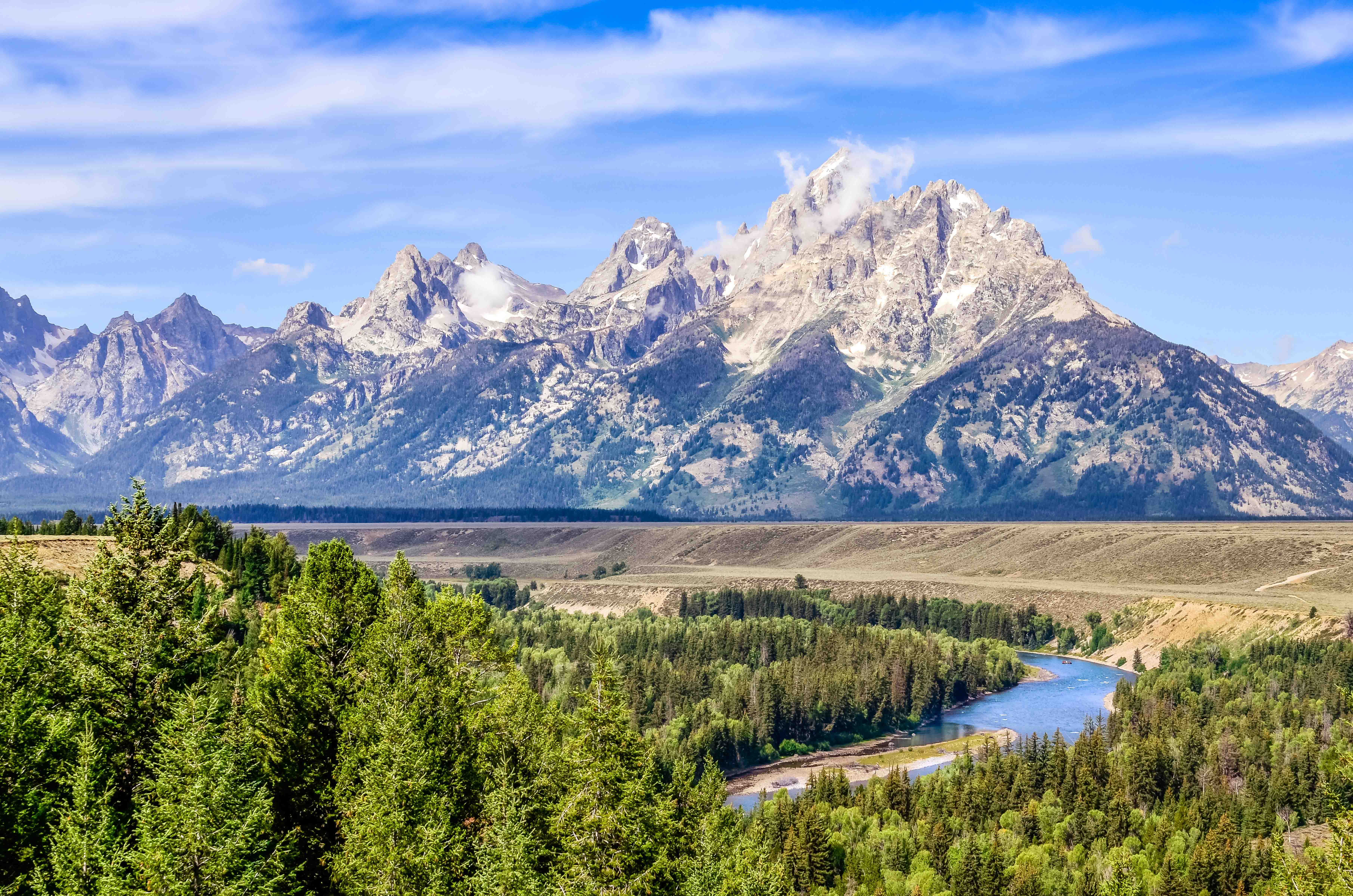 Trip to Jackson Hole - View of the Teton Mountains with river and coniferous forest under a clear blue sky.