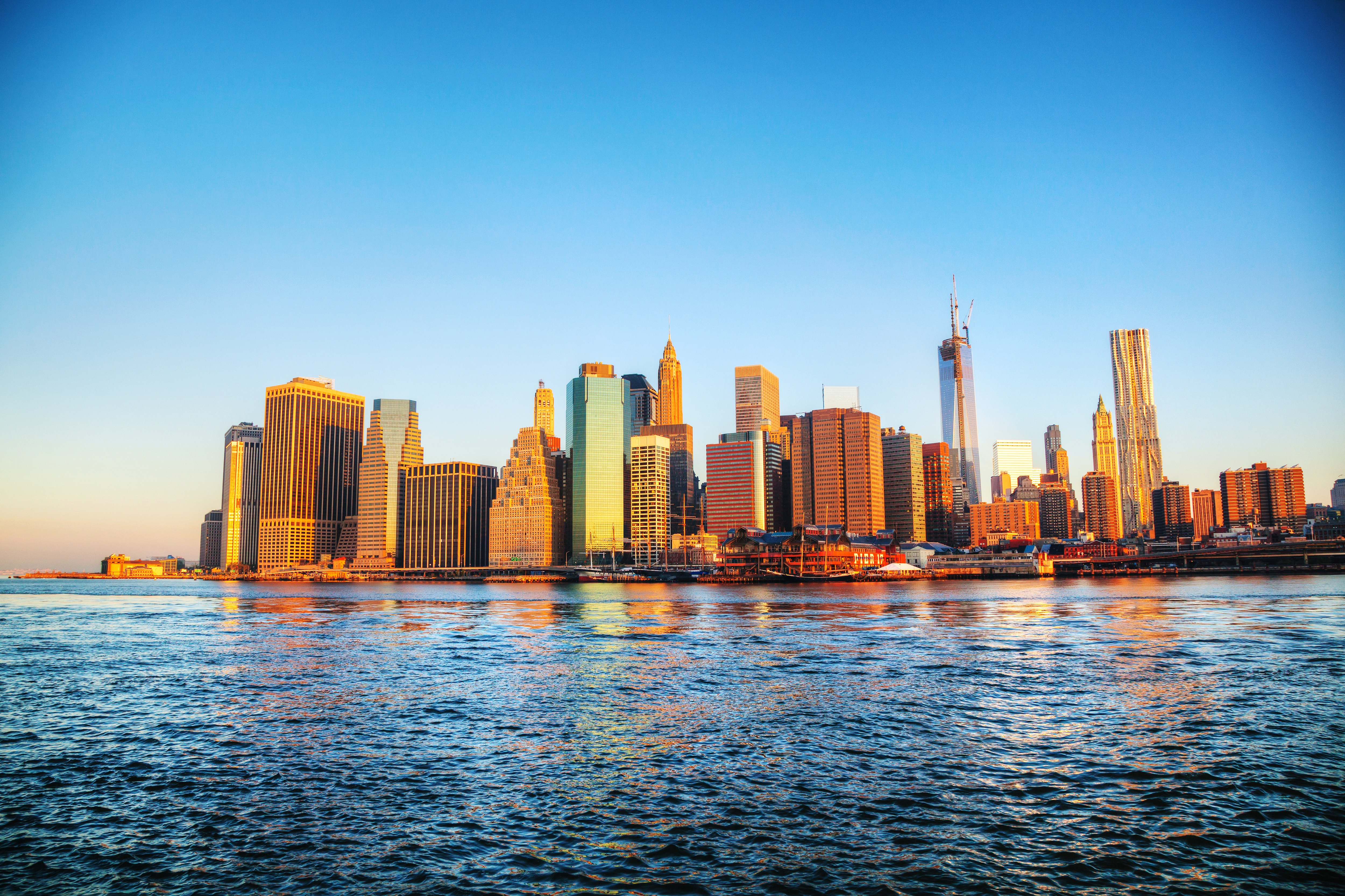 New York City skyline at sunset with skyscrapers reflecting golden light across the Hudson River