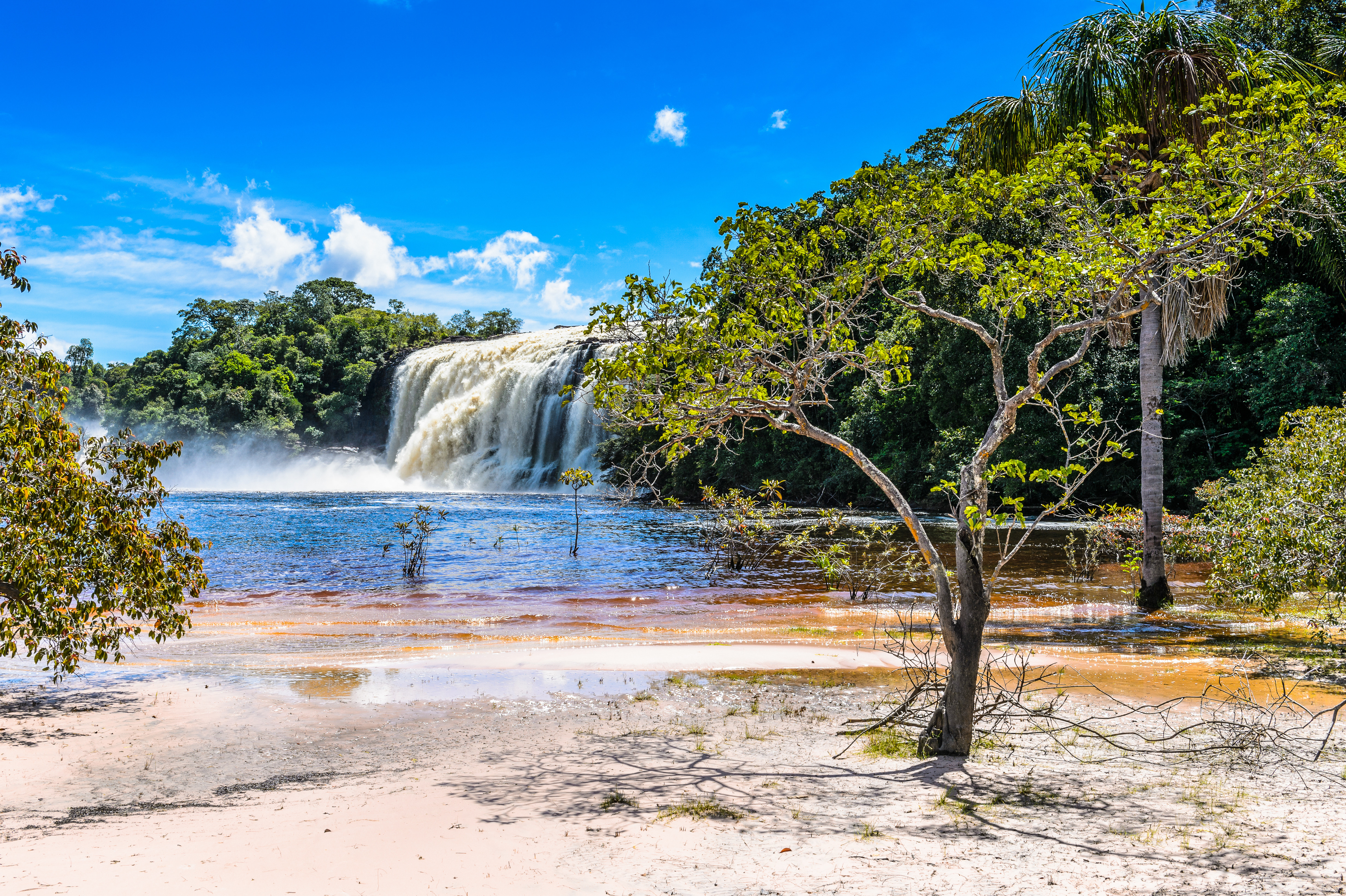 Scenic tropical waterfall surrounded by lush greenery and a clear blue sky in a remote jungle setting