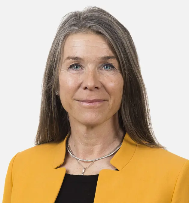 Professionell kvinna med långt grått hår i en gul kavaj, ler mot kameran mot en enfärgad bakgrund
