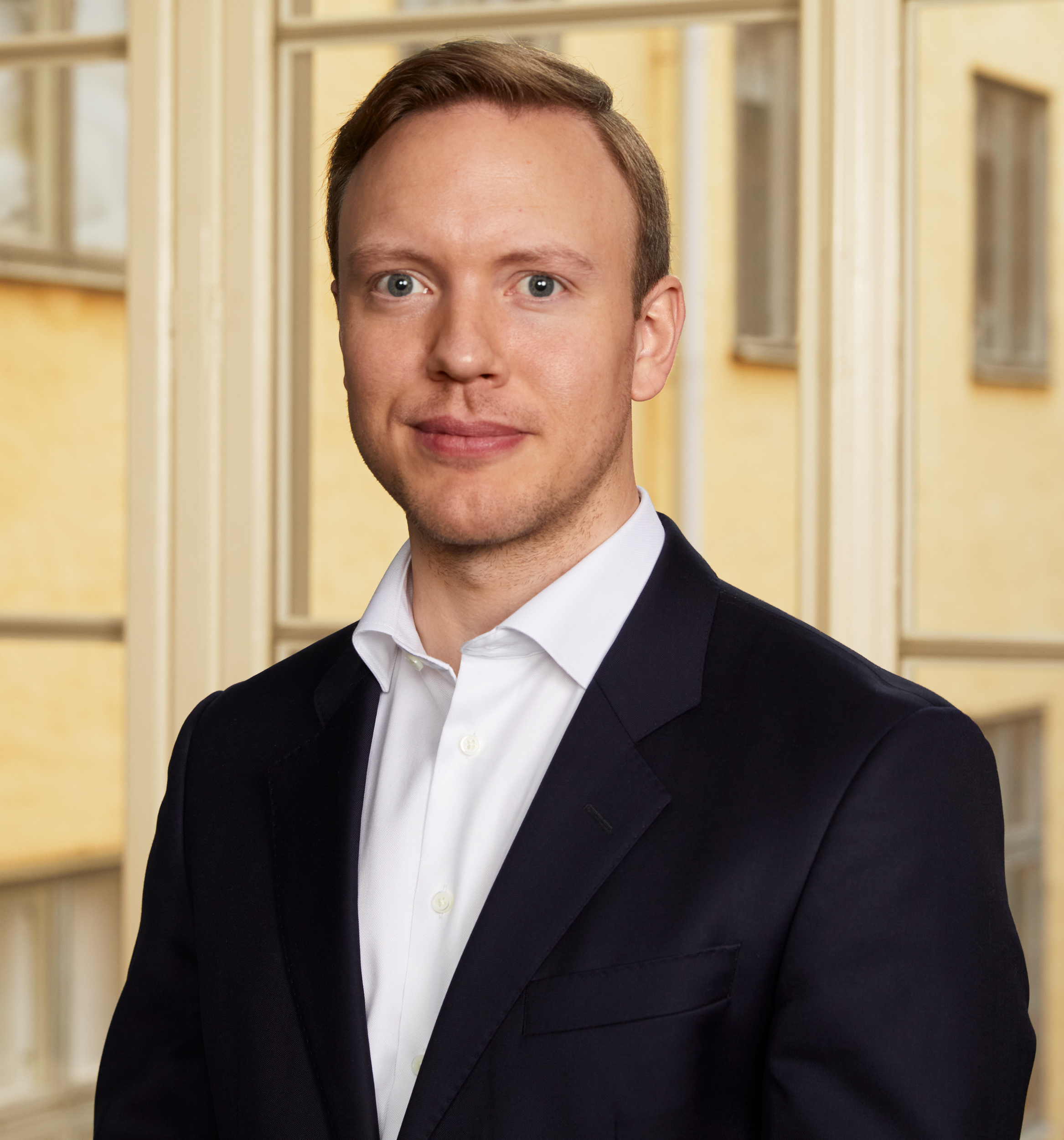 Puvussa oleva henkilö, jolla oli lyhyet vaaleat hiukset, sumean rakennustaustan edessä.