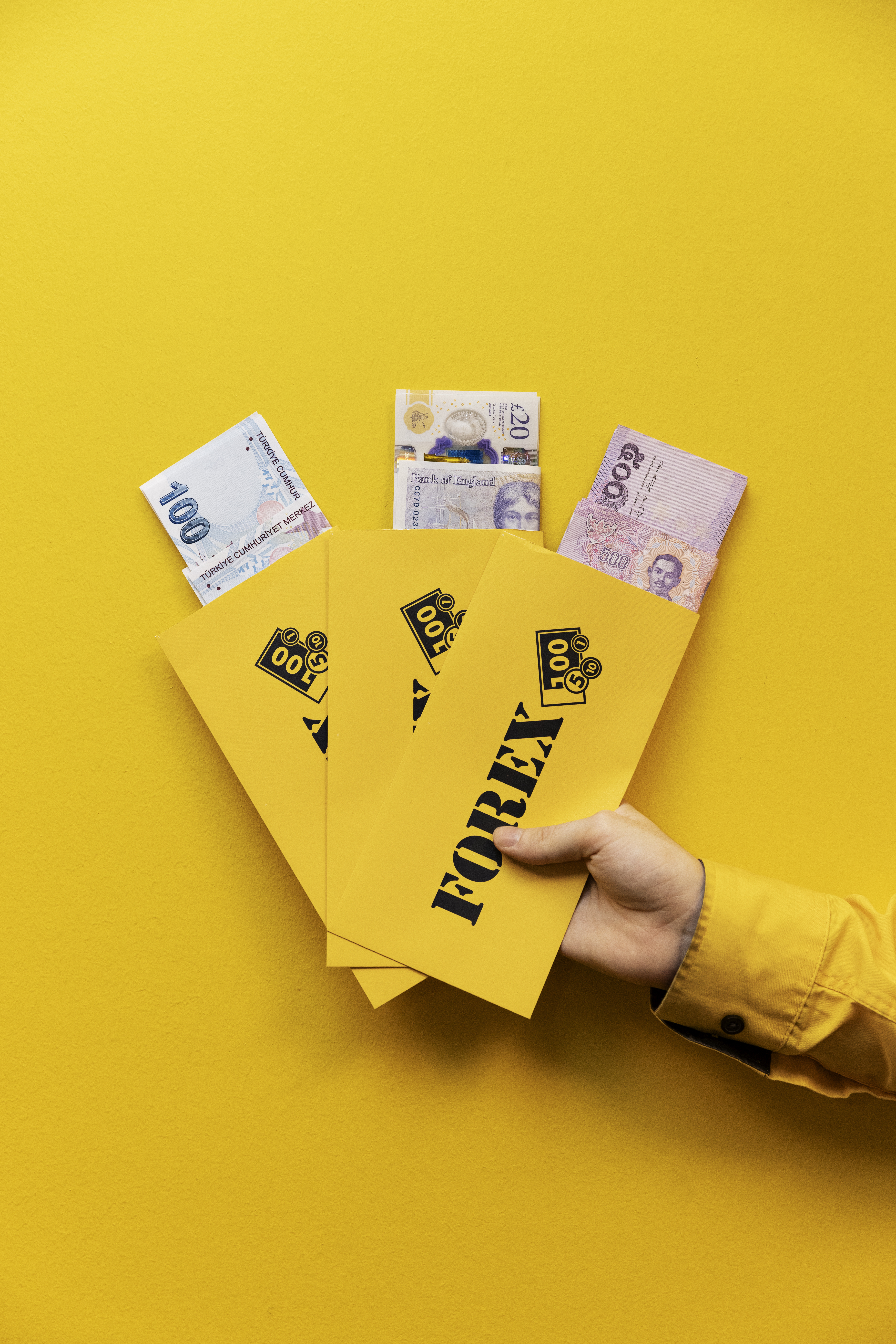 Keltaisia Forex-kirjekuoria, joissa on erilaisia seteleitä, keltaisella taustalla.