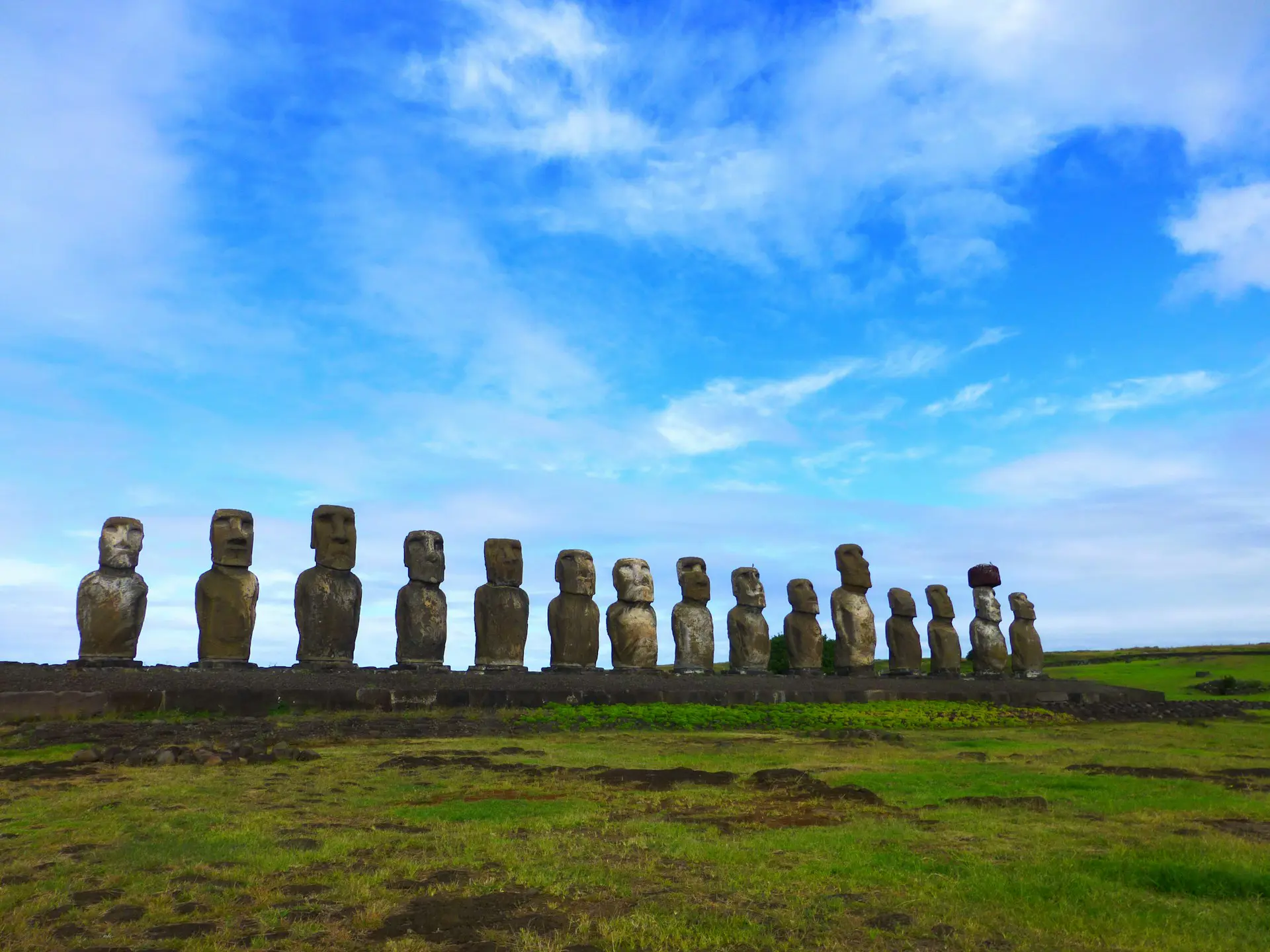Rapa Nui -saarella sijaitsevat Moai-patsaat nurmikolla pilvistä ja sinistä taivasta vasten